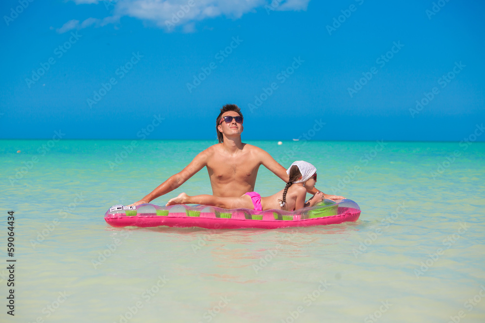 Young father with cute daughter on an air mattress in the sea