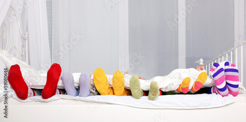 Happy family in colorful socks on white bed.