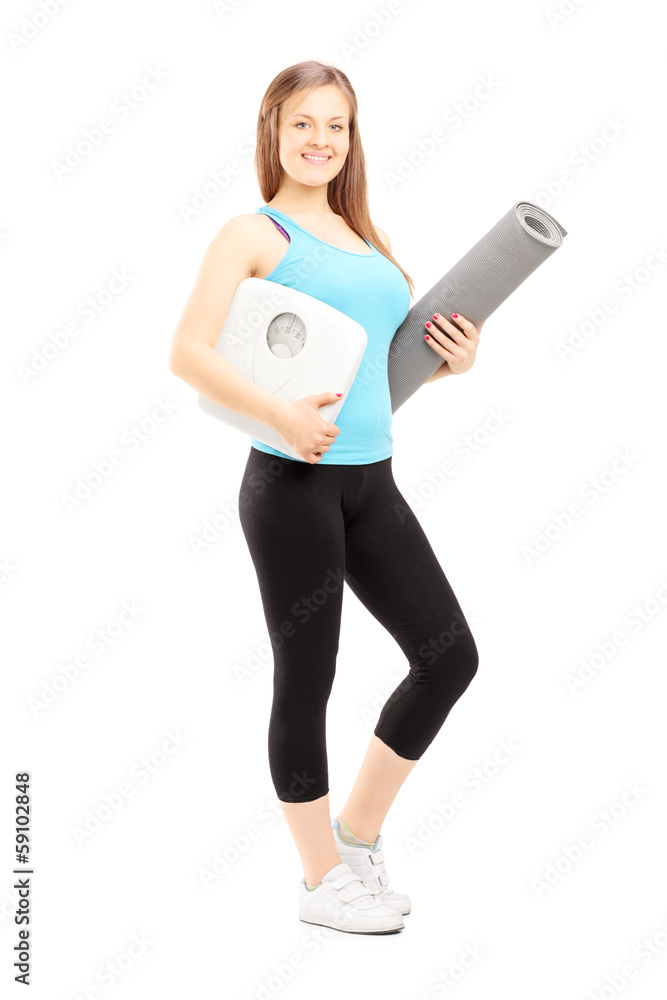 Smiling female athlete holding a weight scale and mat Smiling female athlete holding a weight scale and mat