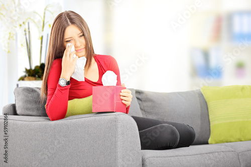 Sad female seated on a sofa wiping her eyes from crying photo