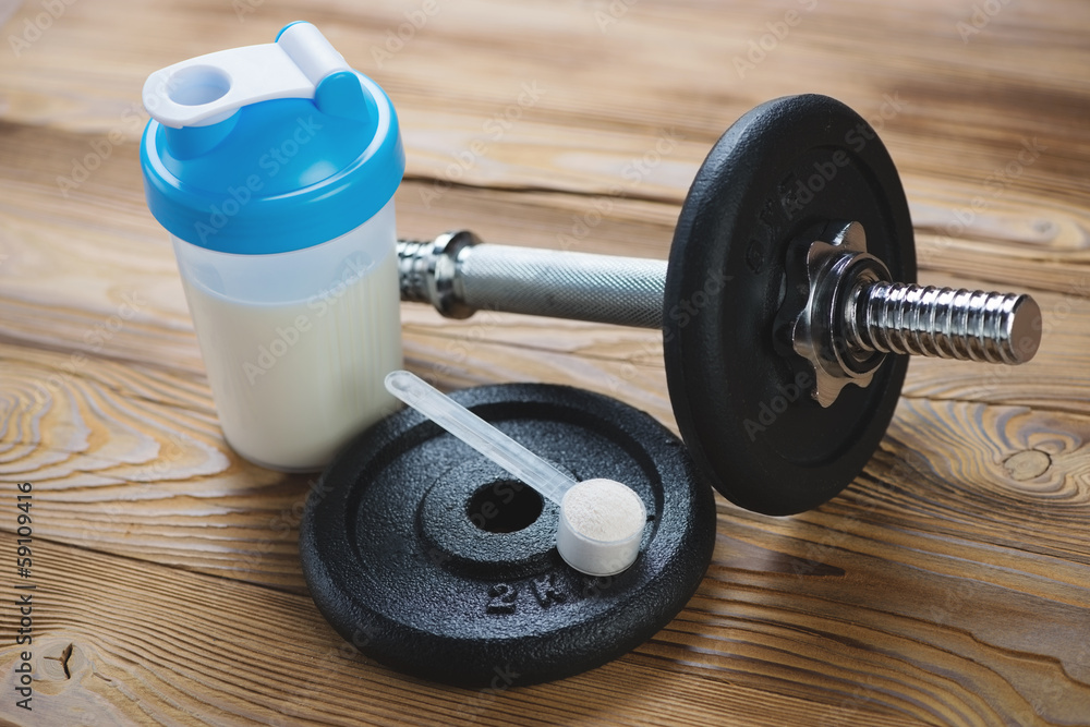 Shaker with protein and a dumbbell over a wooden background Shaker with protein and a dumbbell over a wooden background