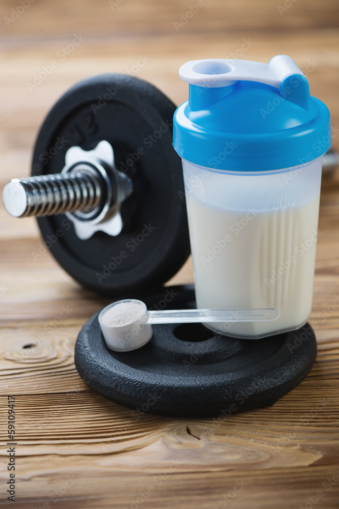 Vertical shot of protein shake, measuring scoop and a dumbbell Vertical shot of protein shake, measuring scoop and a dumbbell
