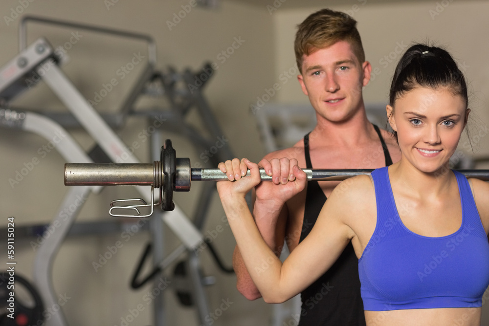 Male trainer helping fit woman to lift the barbell in gym Male trainer helping fit woman to lift the barbell in gym