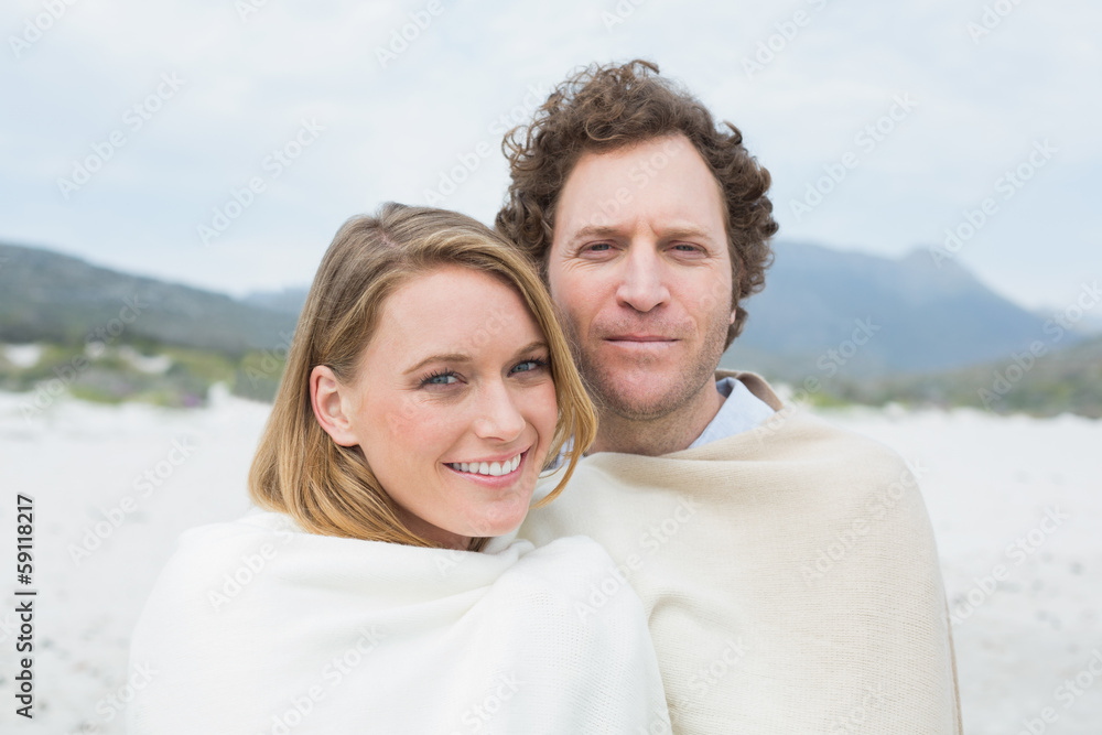 Smiling couple wrapped in blanket at beach