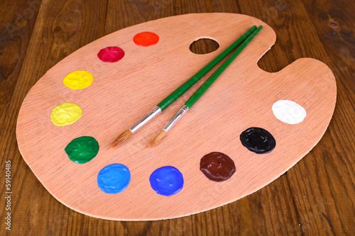 Wooden art palette with paint and brushes on table close-up