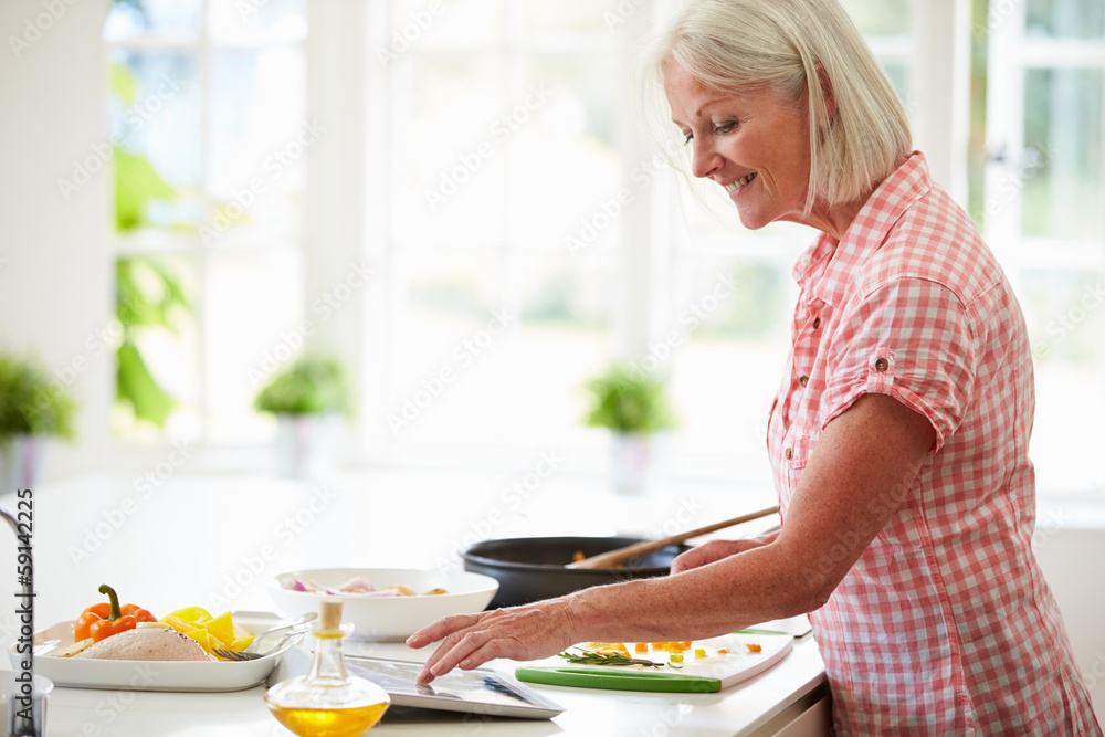 Middle Aged Woman Following Recipe On Digital Tablet Middle Aged Woman Following Recipe On Digital Tablet