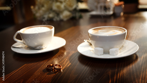 Two cups of coffee on the table  with wedding rings.