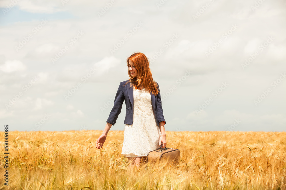 Redhead girl with suitcase at spring wheat field.