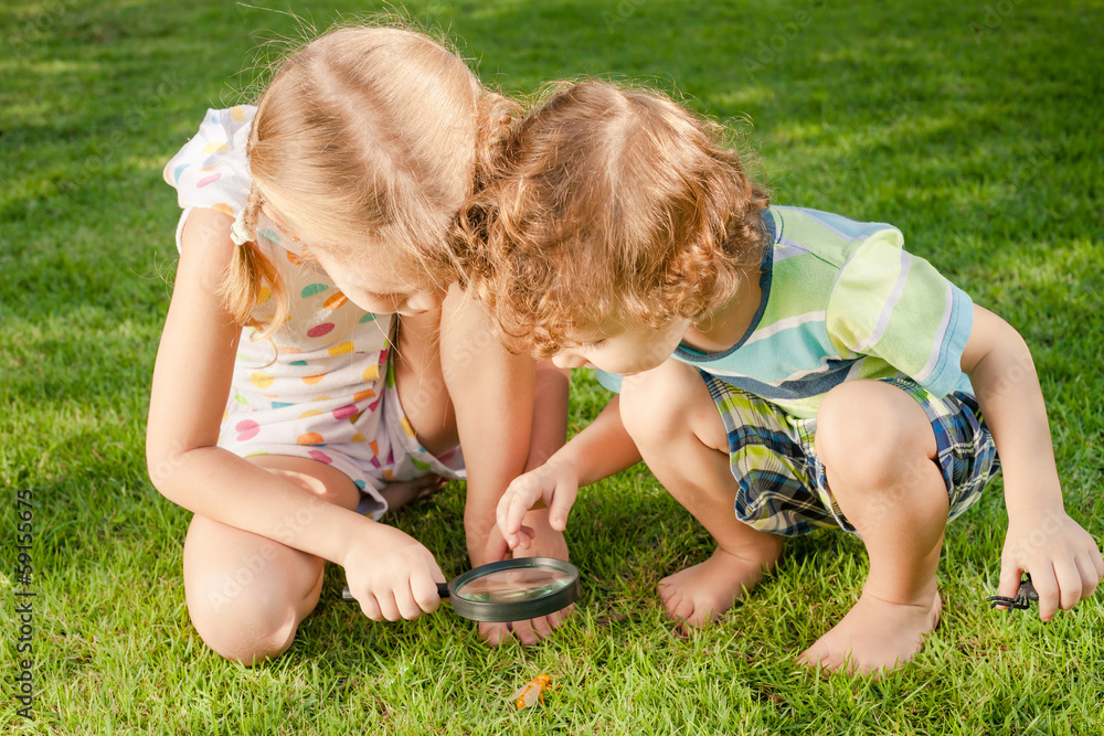 Two little kids playing with magnifying glass outdoors in the d Two little kids playing with magnifying glass outdoors in the d