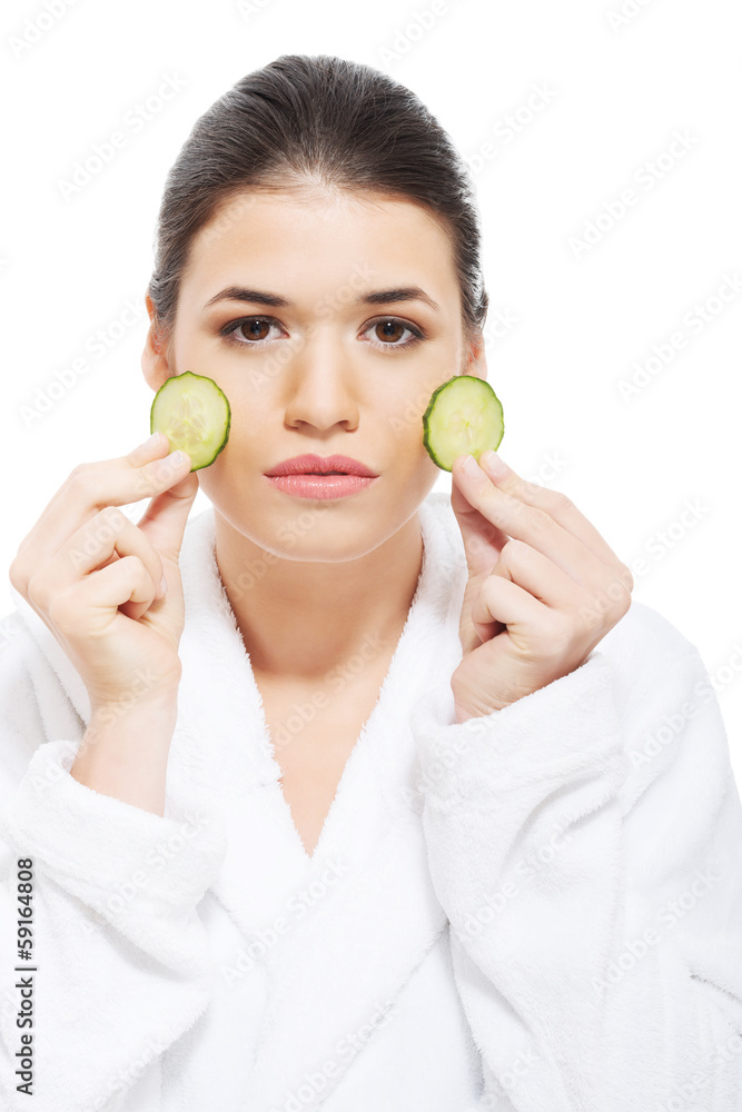 Beautiful woman in bathrobe holding slices of cucumber.