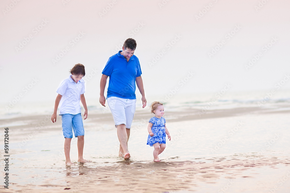 Young father with his son and toddler girl walking at the beach