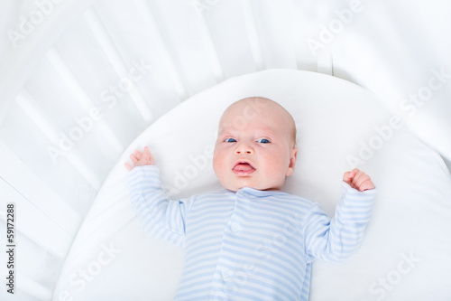 Sweet newborn baby boy in a white round crib photo