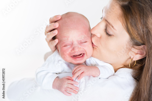 Young mother kissing her crying newborn baby