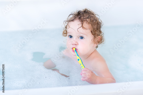 Adorable baby girl with big blue eyes brushing her teeth taking