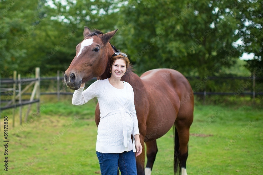 Attractive young pregnant woman and a horse standing in a field Attractive young pregnant woman and a horse standing in a field