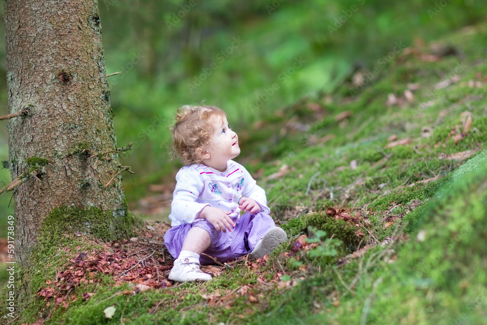 Cute curly baby girl playing in a beautiful pine wood forest in Cute curly baby girl playing in a beautiful pine wood forest in