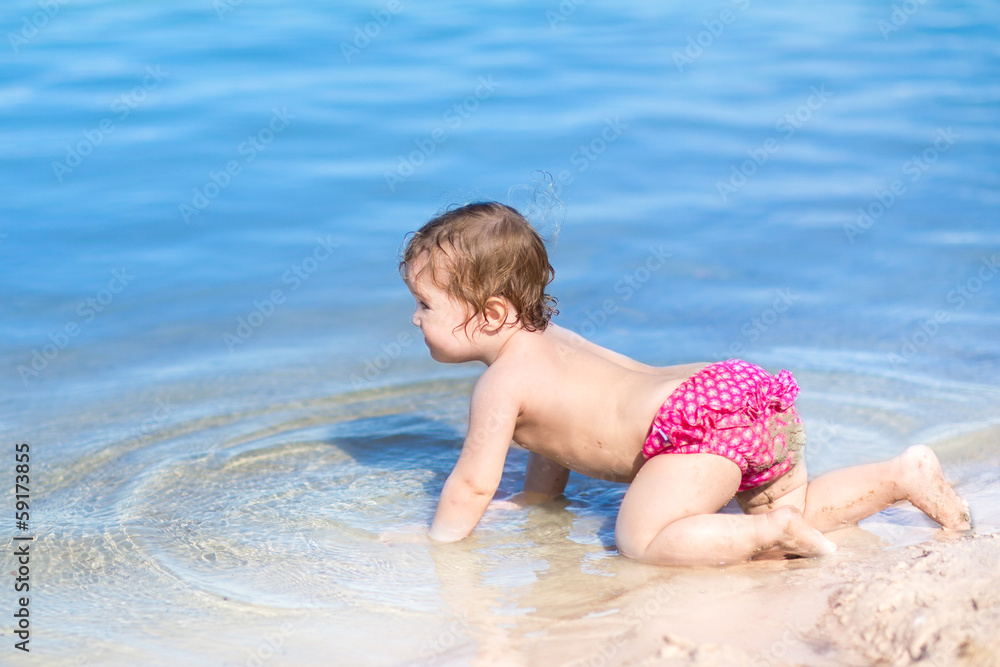 Cute little baby crawling on a beach with clear blue water Cute little baby crawling on a beach with clear blue water