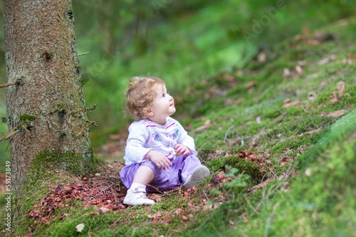 Cute curly baby girl playing in a beautiful pine wood forest in
