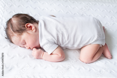 Tiny newborn baby sleeping on a white knitted blanket