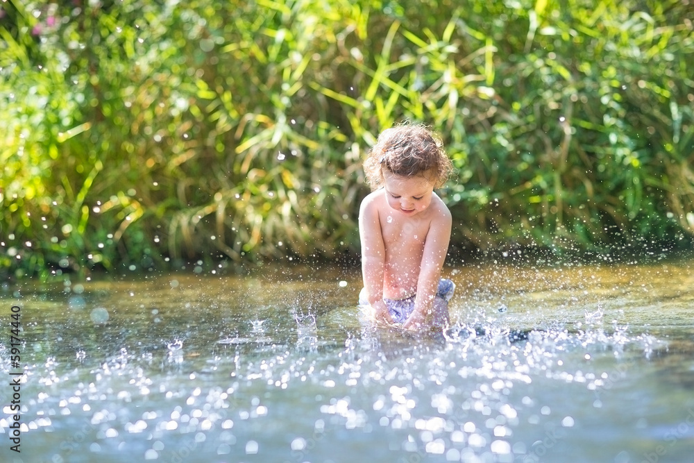 Curly baby girl splashing in a river on a sunny warm day Curly baby girl splashing in a river on a sunny warm day