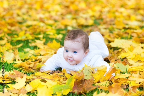 Laughing baby girl playing in an autumn park on yellow leaves