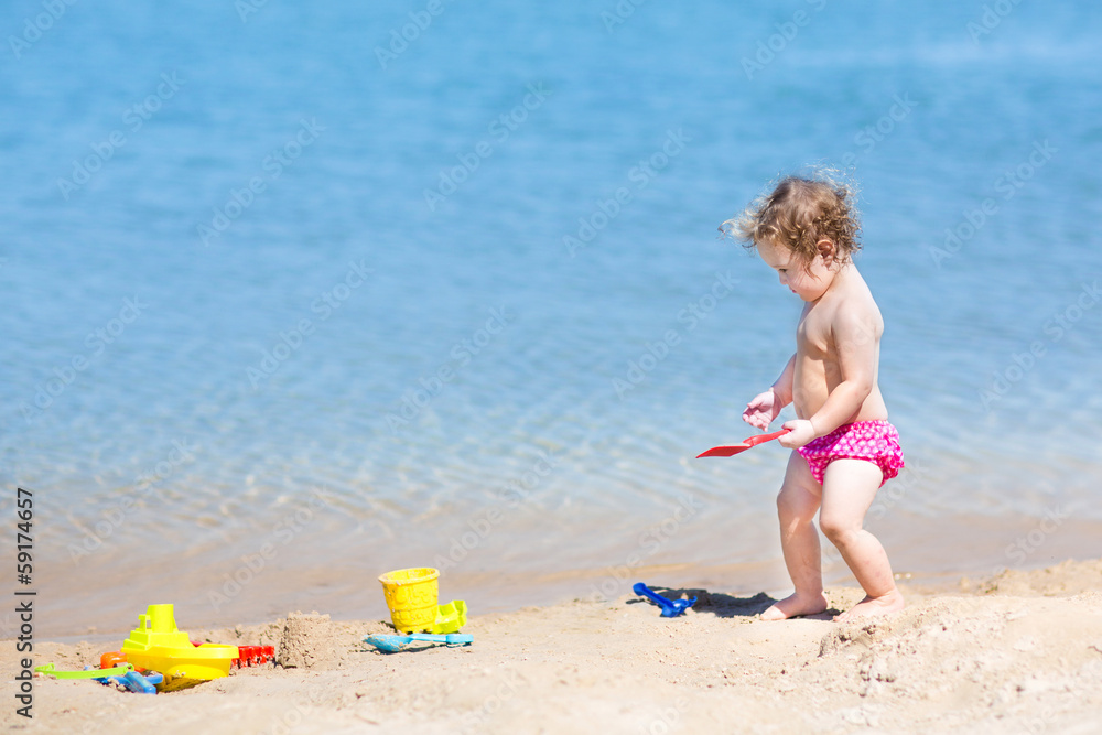 Adorable baby girl with curly hair playing on a beach Adorable baby girl with curly hair playing on a beach