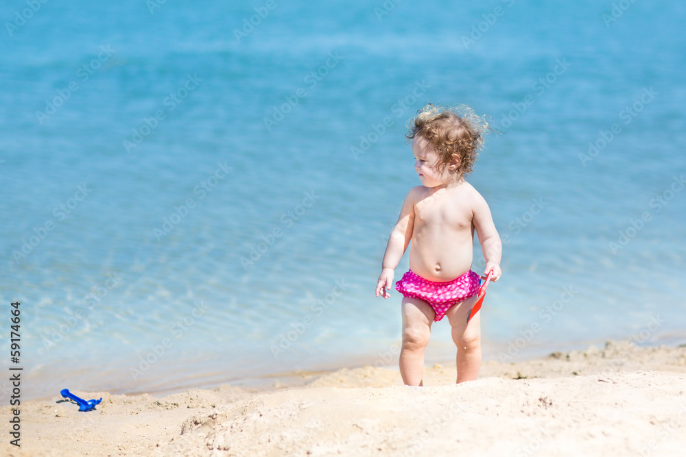 Cute funny baby girl with curly hair playing in sand on a beach Cute funny baby girl with curly hair playing in sand on a beach