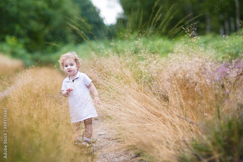 Adorable curly baby girl walking in high grass in an autumn park Adorable curly baby girl walking in high grass in an autumn park