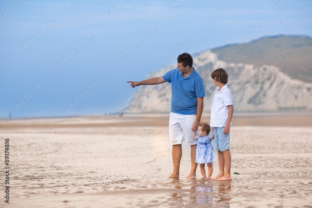 Young father playing with his son and baby daughter on a beach