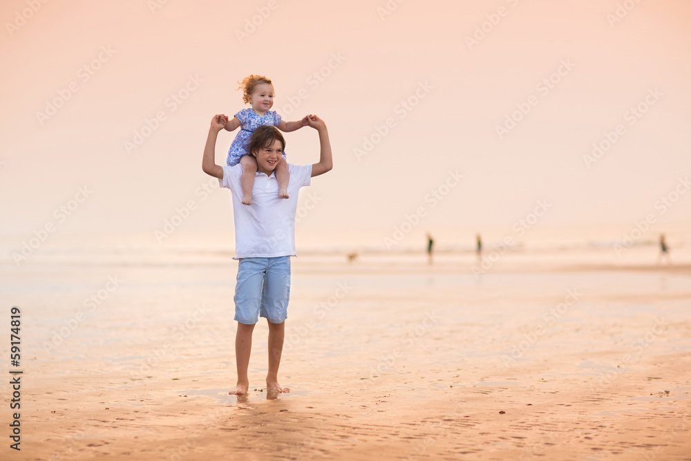 Brother and baby sister playing on a beautiful beach at sunset Brother and baby sister playing on a beautiful beach at sunset