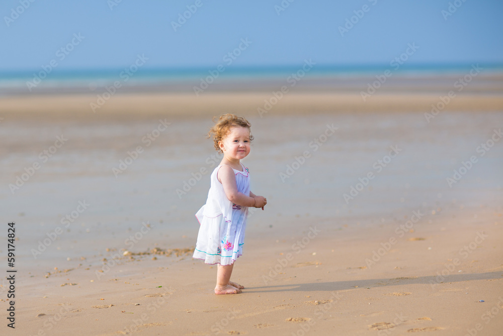 Cute curly baby girl playing on a beautiful tropical beach weari Cute curly baby girl playing on a beautiful tropical beach weari