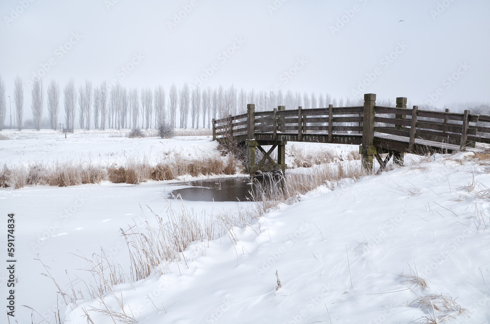 wooden bridge through frozen river in winter wooden bridge through frozen river in winter
