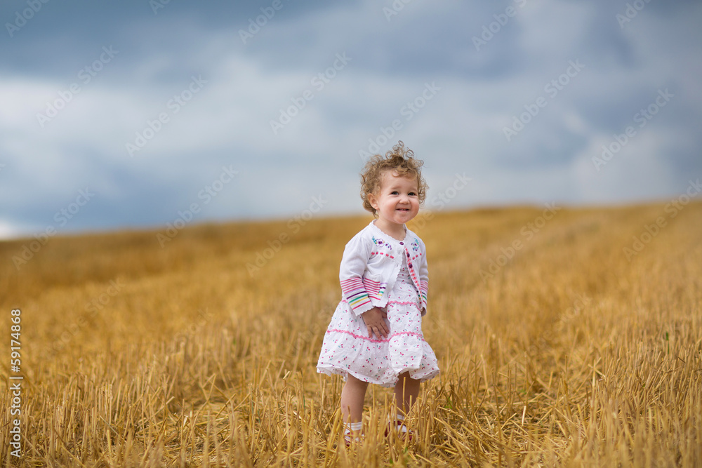 Curly baby girl walking in a golden wheat field at sunset Curly baby girl walking in a golden wheat field at sunset