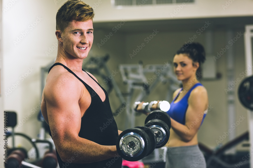 Young man and woman using dumbbells in gym Young man and woman using dumbbells in gym