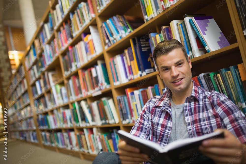 Smiling young student sitting on library floor reading book Smiling young student sitting on library floor reading book