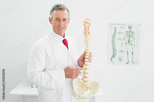 Smiling doctor holding skeleton model in office photo