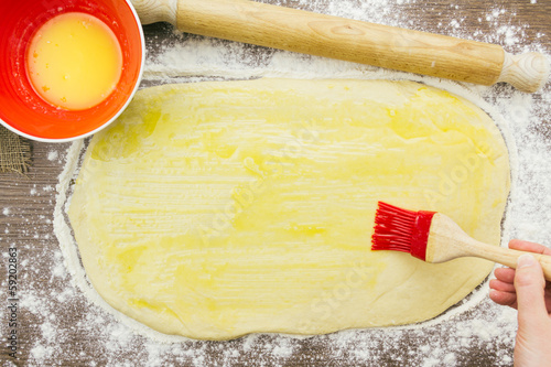 Woman brushing dough with melted butter, above