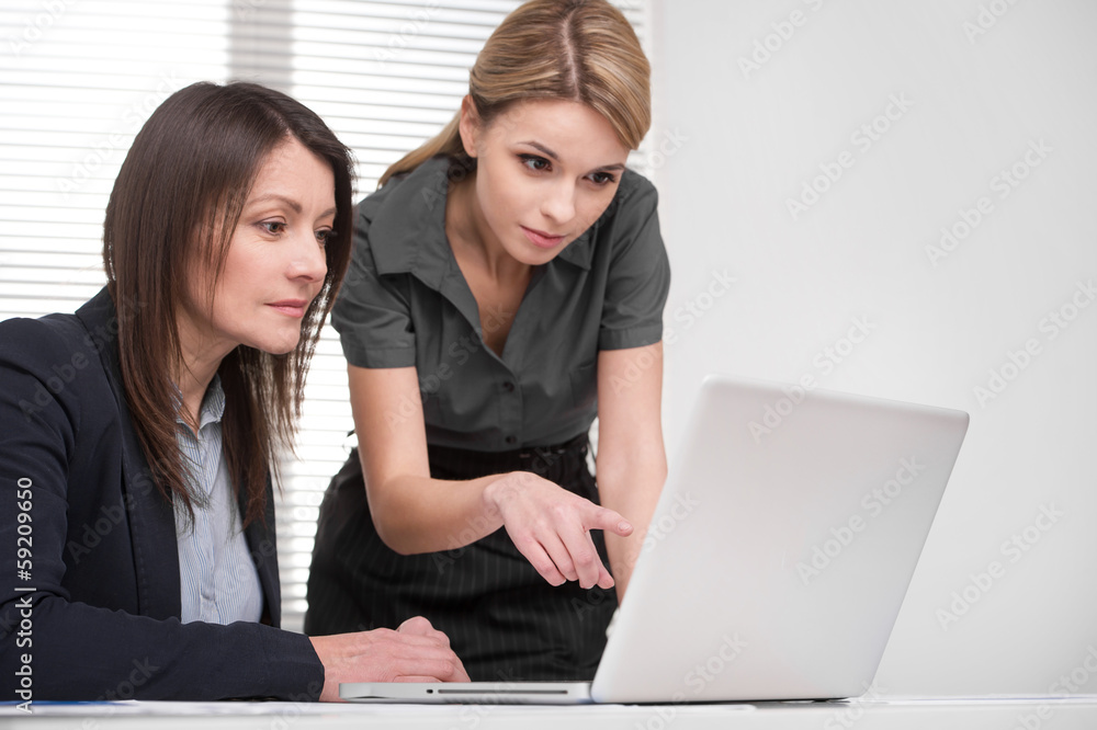 Young blond assistant showing lady boss something on laptop. Young blond assistant showing lady boss something on laptop.