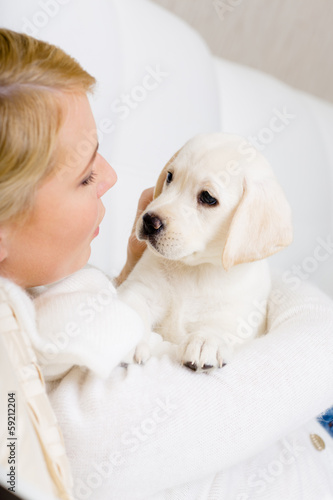 Close up of woman in white sweater embracing white puppy
