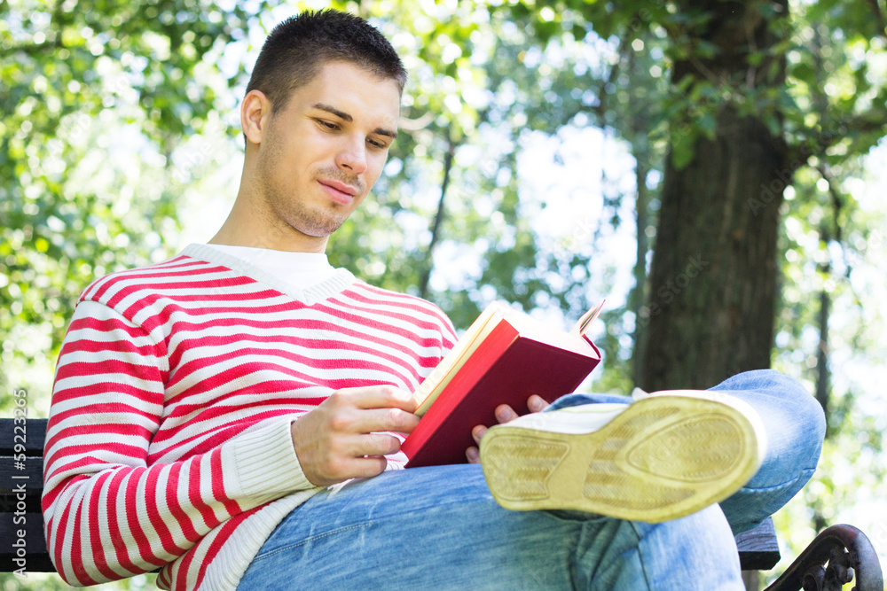 Fototapeta premium Young man reading a book in the park