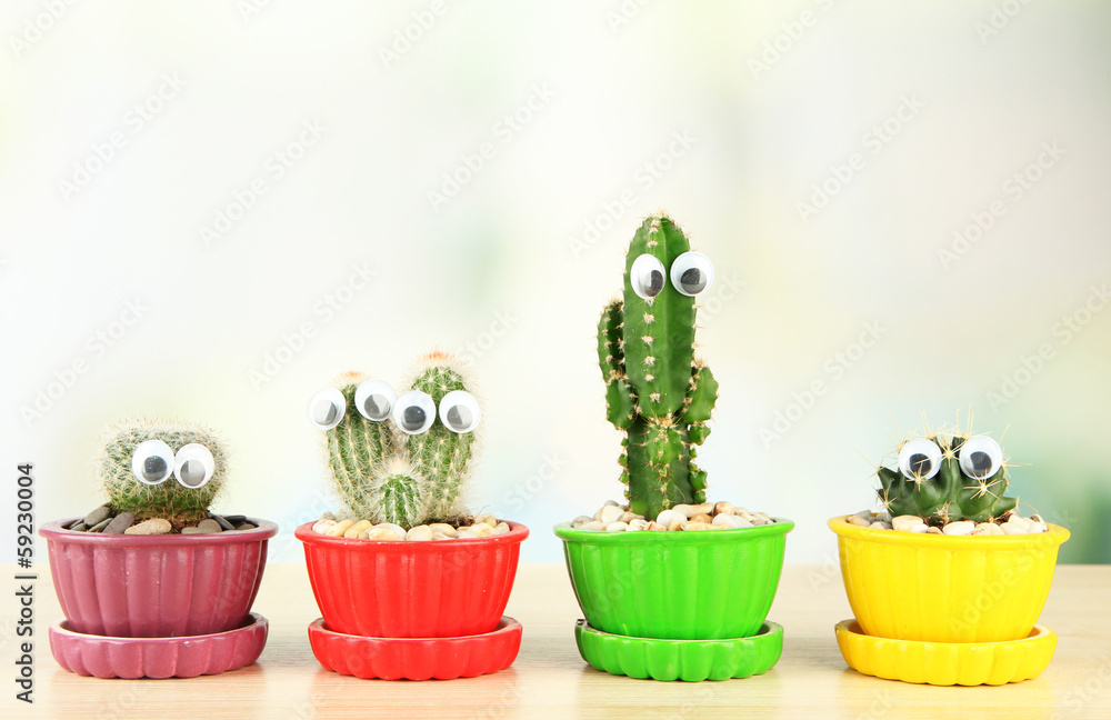Cactuses in flowerpots with funny eyes, on wooden table