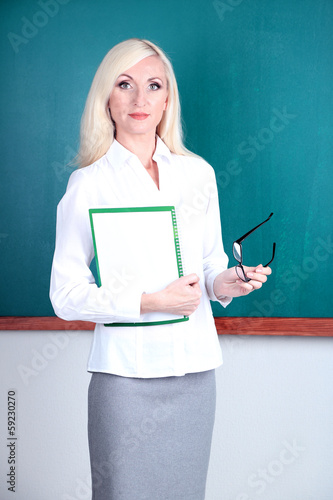 School teacher near blackboard with folder in classroom