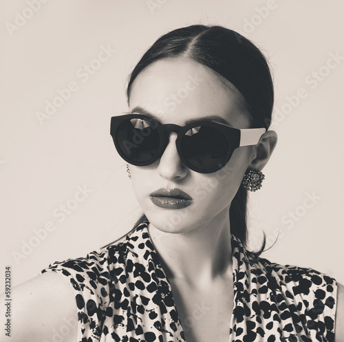 The fashionable young woman in sunglasses posing