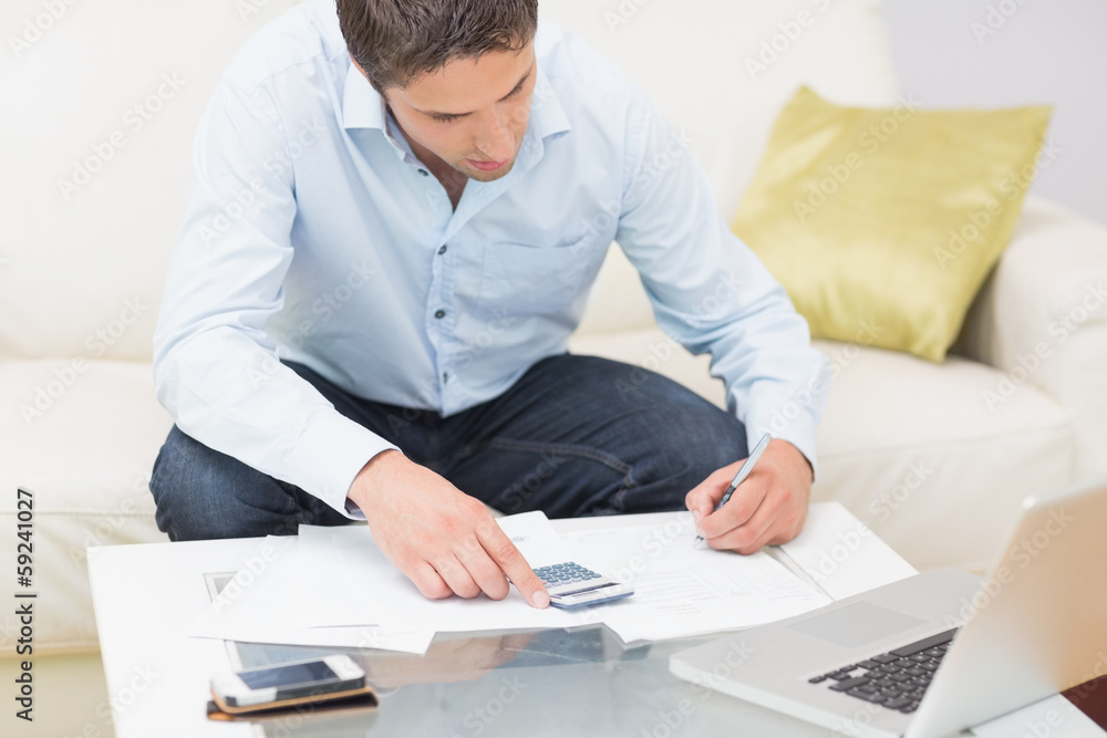 Young man with bills, calculator and laptop at home