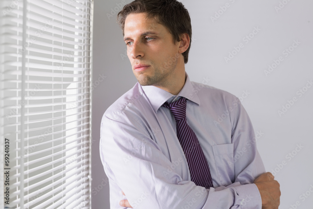 Serious businessman peeking through blinds in office Serious businessman peeking through blinds in office