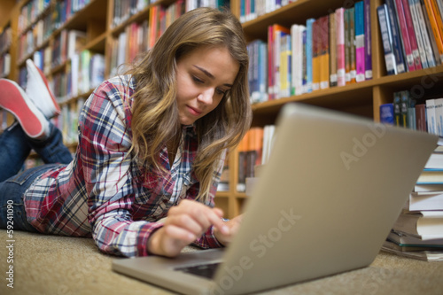 Young happy student lying on library floor using laptop