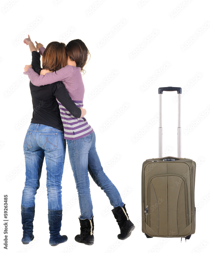 Two women traveling with suitcas and pointing at wall. Two women traveling with suitcas and pointing at wall.