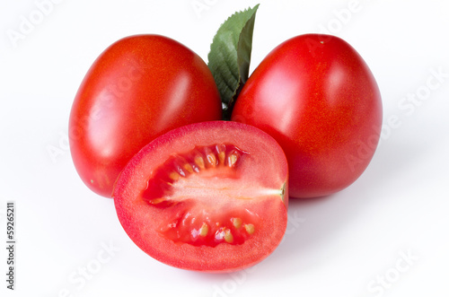 two red ripe plum tomatoes and their cut part inside lying on a white table Close-up on full frame isolated on white background