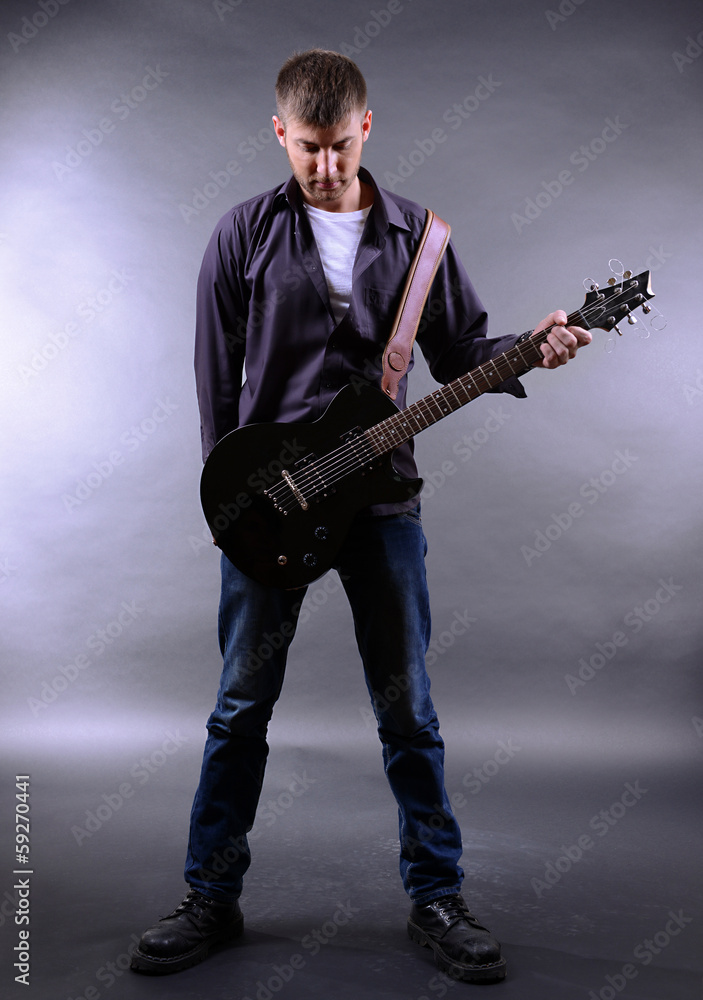 Fototapeta premium Young musician playing guitar on gray background