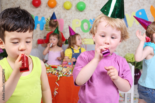 Two little boys blow in multicolor party blowers at birthday